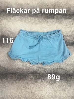 Blå shorts med volangkant och snörning - Söta ljusblå shorts med volangkant och snörning i midjan. Perfekta för varma dagar och har en avslappnad passform. 🌸 Fläckar på rumpan. Storlek 116. 