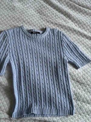 Ljusblå kabelstickad topp Gina Tricot - Säljer en ljusblå kabelstickad topp från Gina Tricot. Tröjan har korta ärmar, rund halsringning och ribbade kanter. Perfekt för dig som gillar en clean och stilren look med en twist av klassiskt stickat mönster.