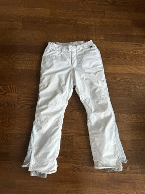 Vita skidbyxor från Marmot - Säljer ett par vita skidbyxor från Marmot med raka ben och förstärkta benslut. Byxorna har resår i midjan och dragkedja med knapp framtill. Perfekta för vintersport och outdoor-äventyr. Materialet är slitstarkt och vattenavvisande.