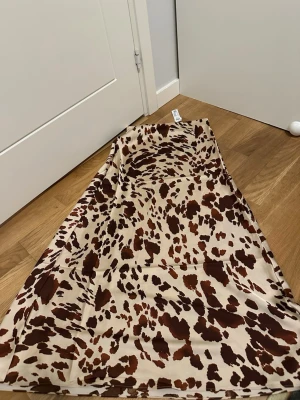 Beige satinkjol med leopardmönster - Säljer en beige långkjol i satin med brunt leopardmönster. Kjolen har en mjuk, glansig yta och ett flytande fall som ger en snygg siluett. 