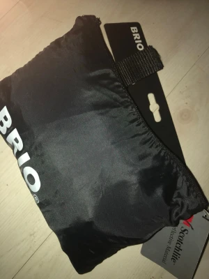 Svart väska från BRIO. regnskydd  till  - Regnskydd Säljer en svart väska från BRIO i smidig, lätt nylon med dragkedja och praktisk rem. Perfekt att ha med sig när man behöver extra förvaring. Enkel och stilren design med BRIO-logga på sidan.