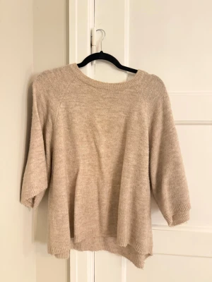 Beige stickad tröja med trekvartsärm - Mysig beige stickad tröja med rund halsringning och trekvartsärmar. Tröjan har en avslappnad passform och ribbstickade muddar vid ärmslut och nederkant. Perfekt för lager-på-lager och enkel att matcha med olika outfits.passar xs-m 