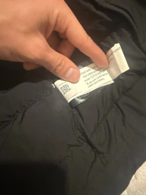 Svart dunjacka från The North Face - Säljer en svart dunjacka från The North Face med huva och klassisk pufferstil. Jackan är quiltad och har långa ärmar samt dragkedja framtill. Perfekt för kalla dagar och enkel att matcha med olika outfits.