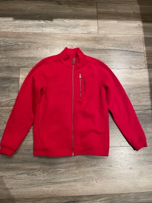 Sail racing hoodie - Riktigt snygg röd fleecejacka från sail racing med hel dragkedja och hög krage. Jackan har en bröstficka med dragkedja och diskret logga på bröstet. Perfekt för lager-på-lager och chill dagar.