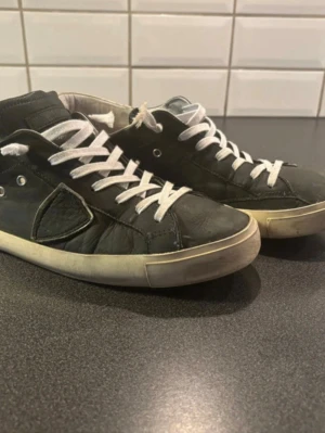 Philippe Model svarta sneakers - Svarta låga sneakers från Philippe Model med vita snören och vit sula. Skorna har en klassisk design med läderdetaljer och diskret logga på sidan. Perfekta för en avslappnad och stilren look.