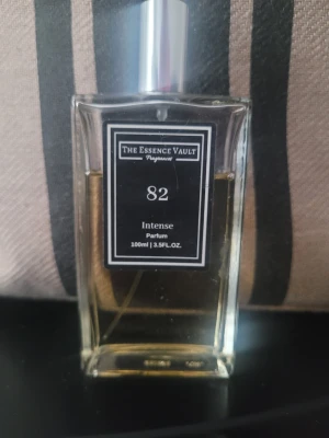 The Essence Vault 82 Intense Parfum - Supergod .   Parfym från The Essence Vault, modell 82 Intense. Flaskan är rektangulär i genomskinligt glas med svart etikett och silverfärgad spraykork. Innehållet är gyllene och flaskan rymmer 100 ml. En stilren och modern doft för dig som gillar exklusiva parfymer.