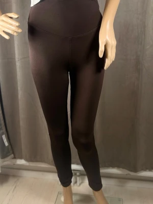 Bruna höga leggings i stretch L-XL - Mörkbruna leggings med hög midja och tight passform. Tillverkade i ett stretchigt material som sitter skönt mot kroppen. Perfekta att styla med oversized tröjor eller crop tops för en trendig look.
