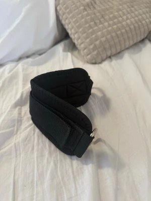 svart brett bälte med metallspänne - säljer en träningsrem för fotled, ett gymtillbehör.