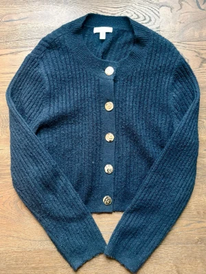 Marinblå ribbstickad kofta med guldknappar - Snygg marinblå ribbstickad kofta med rund hals och fem guldknappar framtill. 