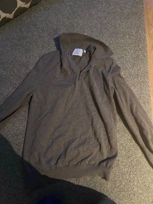 Brun hoodie från Bläck med knappar - Snygg brun hoodie från Bläck i storlek S. Hoodien har en klassisk huva och knappar vid halsen för extra stil. Tillverkad i mjukt och bekvämt material, perfekt för en avslappnad look. Långa ärmar och ribbade muddar ger en skön passform.