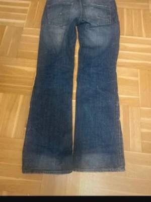 Blå bootcut jeans - Säljer ett par blå bootcut jeans med snygga slitningar och tvättade detaljer. Jeansen har klassisk femficksdesign och låg midja. Materialet är denim i bomull och passformen är avslappnad med utsvängda ben. Perfekta för en avslappnad och trendig look. Midja: 40 innerben:80