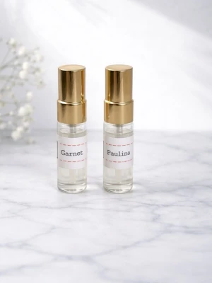 Två parfymer, Granett och Pauling - Säljer två små parfymer i glasflaskor med guldfärgade spraykorkar. Flaskorna har vita etiketter med namnen 'Garnet' och 'Paulina' tryckta på. Perfekt storlek för att ta med i väskan. Den vänstra är lite använ.