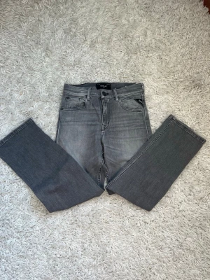 Grå raka jeans från Replay - Snygga grå jeans från Replay med raka ben och klassisk femficksdesign. Jeansen har en tvättad look med subtila slitningar och är tillverkade i ett mjukt denimtyg. Perfekta för dig som gillar en avslappnad men stilren vibe.