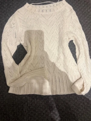 Vit kabelstickad tröja - Säljer en vit kabelstickad tröja med rund hals och långa ärmar. Tröjan har ett snyggt mönster med hålstickning och bred ribbad kant nedtill. Perfekt för dig som gillar klassisk och stilren stickad design.
