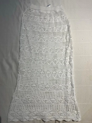 Vit virkad långkjol - Säljer en vit virkad långkjol med snyggt hålmönster och elastisk midja. Kjolen har ett bohemiskt uttryck och är perfekt för varma dagar. Passar dig som gillar en avslappnad men ändå trendig stil.
