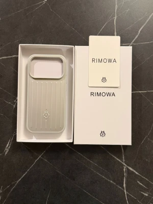 Rimowa iphone 17 pro  - Snyggt och stilrent mobilskal från Rimowa i silverfärgad hårdplast med klassiska räfflade linjer och logga på baksidan. Skalets design är inspirerad av Rimowas ikoniska resväskor och ger din mobil en exklusiv look.
