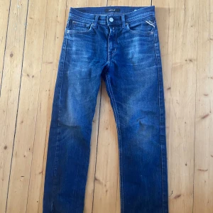 Replay Jeans Thad - Snygga blå jeans från Replay i klassisk rak modell. Jeansen har fem fickor, gylf med knapp och dragkedja samt diskreta slitningar för en cool look. Sällan använda och i fint skick. Modellen heter Thad.
