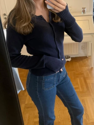 Mörkblå ribbad kofta - Snygg mörkblå kofta med ribbade muddar och knappar framtill. Modellen är figurnära och har långa ärmar. Perfekt att styla med jeans för en enkel och clean look.