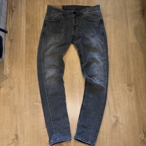Grå jeans från Dondup, storlek 33 - Snygga grå jeans från dondup med tvättad look och diskreta slitningar på benen. Modellen har raka ben och klassiska fem fickor. Bakfickorna har unik broderad detalj och en svart patch med vita ögon. Perfekta för dig som gillar streetwear med edge.