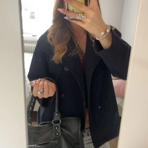 Marinblå kappa från Gina Tricot - Snygg marinblå kappa från Gina Tricot med klassisk krage och knäppning framtill. Jackan har en stilren och tidlös design som passar perfekt till många outfits. Materialet känns mjukt och håller värmen under kyligare dagar. Storlek 158/164 passar en S