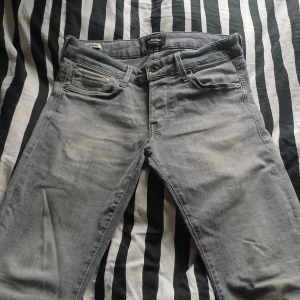Grå slim jeans Jack & Jones Glenn - Snygga grå jeans från Jack & Jones, modell Glenn med slim fit. Klassisk femficksdesign och bekväm passform. Jeansen är tillverkade i mjukt denimtyg och har en stilren look som passar till det mesta. Perfekta för dig som gillar en smalare siluett.