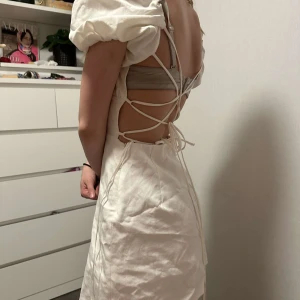 Vit klänning med öppen rygg - Supersöt vit klänning med puffiga korta ärmar med öppen rygg och snörning. Materialet känns som linne och ger en fräsch sommarkänsla.