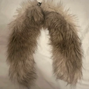 Beige fuskpäls krage med spänne - Supermjuk och fluffig beige fuskpäls halsduk från H&M. Insidan är klädd i glansigt tyg med småblommigt mönster i brunt, rött och blått. Perfekt för att ge din outfit en extra cozy och trendig touch under kyliga dagar