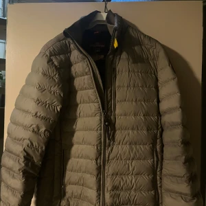 Grå lättviktsdunjacka Parajumpers M - Säljer en grå, quiltad lättviktsdunjacka från Parajumpers i storlek M. Jackan har dragkedja framtill, hög krage och två sidofickor med dragkedja. Perfekt för dig som vill ha en stilren och funktionell jacka med sportig vibe.
