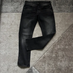 G-Star RAW 3301 Slim svarta jeans - Svarta jeans från G-Star RAW, modell 3301 Slim. Jeansen har en snygg tvättad look med diskreta slitningar, klassiska fem fickor och läderpatch bak i midjan. Slim fit och  Perfekta för dig som gillar stilrena och coola jeans.