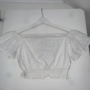 Vit croppad blus  - Superfin vit croppad blus från SHEIN med broderade detaljer och smockad midja. Toppen har korta puffärmar och offshoulder-modell, perfekt för en söt och somrig look. Materialet är lätt och luftigt, och spetskanten upptill ger en extra gullig touch.