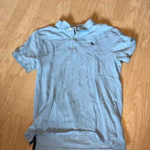 Ljusblå pikétröja från H&M - Säljer en ljusblå pikétröja från H&M i storlek 158/164. Tröjan har klassisk krage, knappar vid halsen och en liten broderad logga på bröstet. Perfekt för en chill och stilren look.