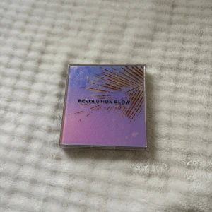 Revolution Glow ögonskuggspalett - Snygg ögonskuggspalett från Revolution Glow med 9 pigmentrika nyanser i guld, beige, koppar, röd, vinröd, lila och brunt. Paletten har spegel i locket och kommer i ett stilrent, skimrande fodral med palmbladsmotiv. Perfekt för dig som gillar varma och intensiva färger.