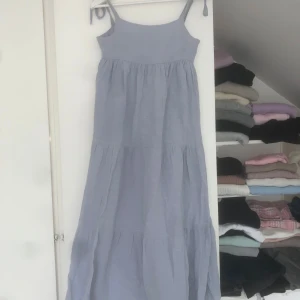 Ljusblå långklänning från Zara - Luftig och flowy ljusblå långklänning från Zara med smala axelband som knyts. Klänningen har flera volanger, perfekt för varma dagar. Enkel och stilren design med avslappnad passform.