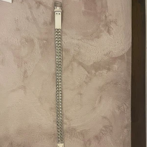 Vitt bälte med silvernitar - Säljer ett vitt bälte med rad av silvriga pyramidnitar längs hela längden. Bältet har klassiskt spänne i metall och är perfekt för att ge din outfit en edgy vibe. Passar till jeans eller kjol för en cool look.