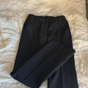 Svarta kostymbyxor med bootcut - Stilrena svarta kostymbyxor från Bik Bok med klassisk bootcut-passform. Byxorna har hällor för bälte, pressveck och två bakfickor. Perfekta för en clean och dressad look. Materialet är slätt och känns bekvämt mot huden.