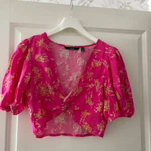 Rosa blommig croppad blus - Superfin rosa blus med blommigt mönster.Modellen är croppad med puffiga korta ärmar, v-ringning och twistad detalj framtill. Perfekt för dig som gillar färg och vill sticka ut lite extra. Tunn och luftig, passar perfekt till sommaren.