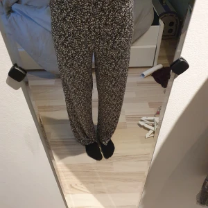 Svarta blommiga wide byxor - Säljer ett par svarta byxor med vitt blommönster. Byxorna har hög midja och ett wide fit, vilket gör dem riktigt sköna och luftiga. Perfekta för dig som gillar en avslappnad och trendig stil. Materialet känns mjukt och följsamt mot huden.
