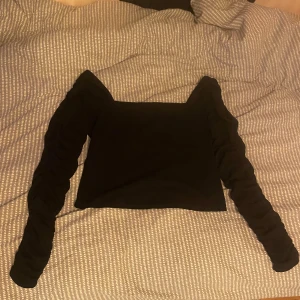 Svart croppad topp med rynkade ärmar H&M - Svart långärmad topp från H&M med croppad passform och fyrkantig urringning. Ärmarna är rynkade längs hela armen vilket ger en cool och trendig look. Perfekt att styla med jeans eller kjol.