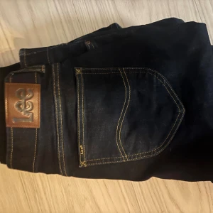 Svarta skinny jeans från Lee - Snygga svarta jeans från Lee med klassisk femficksdesign och kontrastsömmar. Jeansen har en skinny passform och är tillverkade i stretchigt denim för en bekväm känsla. Perfekta för dig som gillar en stilren och enkel look.