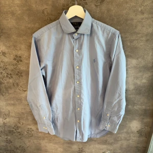 Ralph Lauren Skjorta  - Stilren ljusblå skjorta från Polo Ralph Lauren. Klassisk modell med button-down krage och broderad logga i ton-i-ton på bröstet. Perfekt både till jobbet, middagen eller som snygg casual stil.  Storlek: S, slim fit Skick: Mycket fint skick. Inga fläckar eller hål. Nypris: ca 1 299 kr  Pris: 375 kr eller bud. 