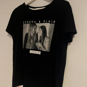 Svart Gossip Girl t-shirt - Svart t-shirt med tryck av Serena & Blair från Gossip Girl. Klassisk rund halsringning och korta ärmar. Skön passform och mjukt material. Trycket har börjat försvinna litegrann men syns fortfarande väldigt tydligt och ser bra ut! Säljer då den tyvärr blivit för liten för mig :( strl är S men den är tajt vid axlarna för mig som brukar bära S vanligtvis