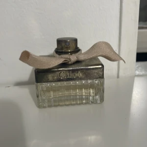 Chloé parfym med rosett - Stilren Chloé-parfym i ikonisk flaska med beige rosett. Perfekt för dig som vill ha en klassisk och trendig accessoar på sminkbordet. Volym och ingredienser syns ej på bilderna.