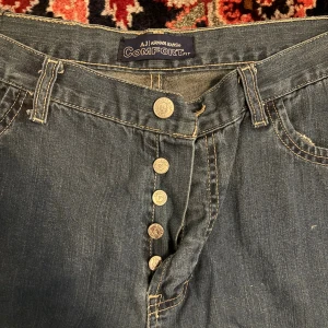 Blå jeans från Armani Jeans - Klassiska blå jeans från Armani Jeans med comfort fit. Byxorna har synliga kontrastsömmar, fem fickor och knäppning med fyra metallknappar framtill. Tillverkade i 100% bomull för en skön känsla. Perfekta för dig som gillar en avslappnad och tidlös look.