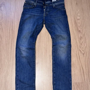 Blå jeans från Jack & Jones - Snygga blå jeans från Jack & Jones med klassisk femficksdesign och knäppning fram. Jeansen har en slim passform och är tillverkade i slitstarkt denimtyg. Perfekta för dig som gillar en tidlös och enkel stil. 