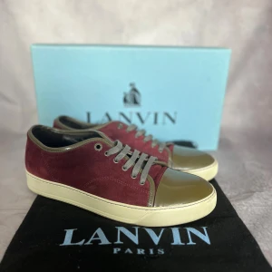 Lanvin Burgundy Suede & Patent Sneakers – EU 41 / UK 7 - Säljer ett par exklusiva sneakers från Lanvin Paris i storlek EU 41 / UK 7. Levereras med originalkartong och dustbag. Nypris ca 5500–6 000 kr.  ✨ Färg: Burgundy mocka med olivgrön patentläder-tå och matchande snörning 📏 Storlek: EU 41 / UK 7 📐 Innermått: ca 26 cm (normal passform för EU 41) ♻️ Skick: Mycket fint begagnat skick (9/10) – sparsamt använda, minimala tecken på slitage 🧵 Material: Mocka, patentläder (lackskinn), gummisula, skinnfoder 