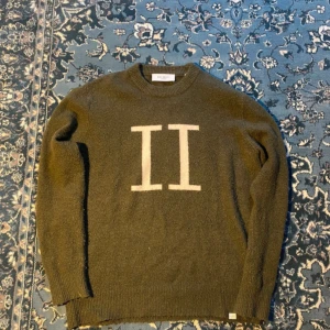 Olivgrön stickad tröja Les Deux M - Snygg olivgrön stickad tröja från Les Deux med stor vit II-logga på bröstet. Tröjan har rund hals, ribbade muddar och lång ärm. Perfekt för dig som gillar stilren design med en twist.