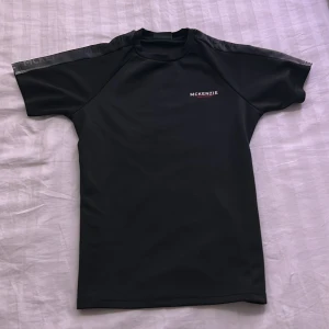 Svart McKenzie t-shirt i polyester - (Använd runt 2 gånger) Säljer en svart t-shirt från McKenzie med sportig vibe. T-shirten har korta ärmar, rund hals och diskret logga på bröstet. Tillverkad i mjukt och lätt polyestermaterial som passar perfekt för träning eller chill dagar.