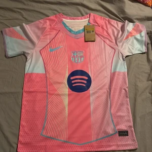 Barça Lamine Yamal rosa Nike tröja S - Säljer en FC Barcelona fotbollströja i rosa och ljusblått från Nike, med Lamine Yamal och nummer 10 på ryggen. Tröjan har korta ärmar, coolt grafiskt mönster och Spotify-logga på bröstet. Tillverkad i 100% polyester, perfekt för dig som älskar Barça.