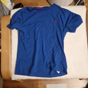 Blå t-shirt från Polo Ralph Lauren - Snygg blå t-shirt från Polo Ralph Lauren med klassisk röd logga broderad på bröstet. T-shirten har rund halsringning och korta ärmar. Tillverkad i mjuk bomull som är skön att ha på sig hela dagen.