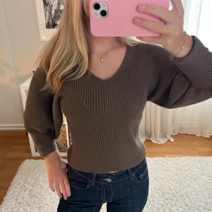 Brun ribbad stickad tröja - Säljer en brun ribbstickad tröja med v-ringning och ballongärmar. Tröjan är croppad och har en snygg, figurnära passform. Perfekt till jeans och enkel att styla🩷